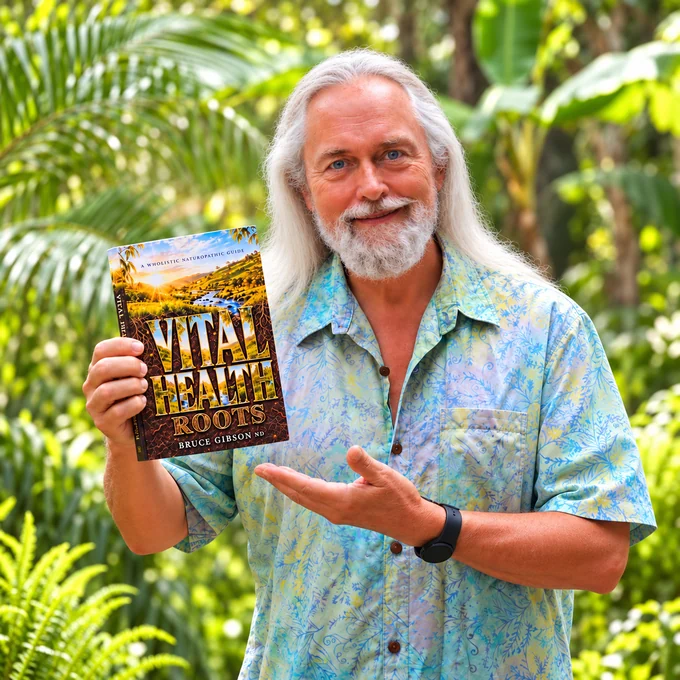 Bruce Gibson smiling in a garden while holding his book Vital Health Roots